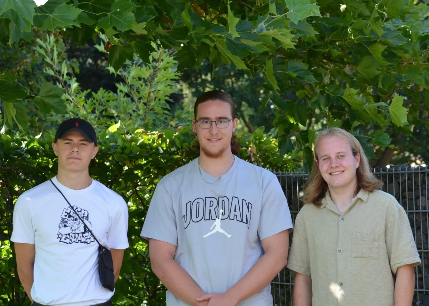Drei junge Männer vor einer Hecke im Garten