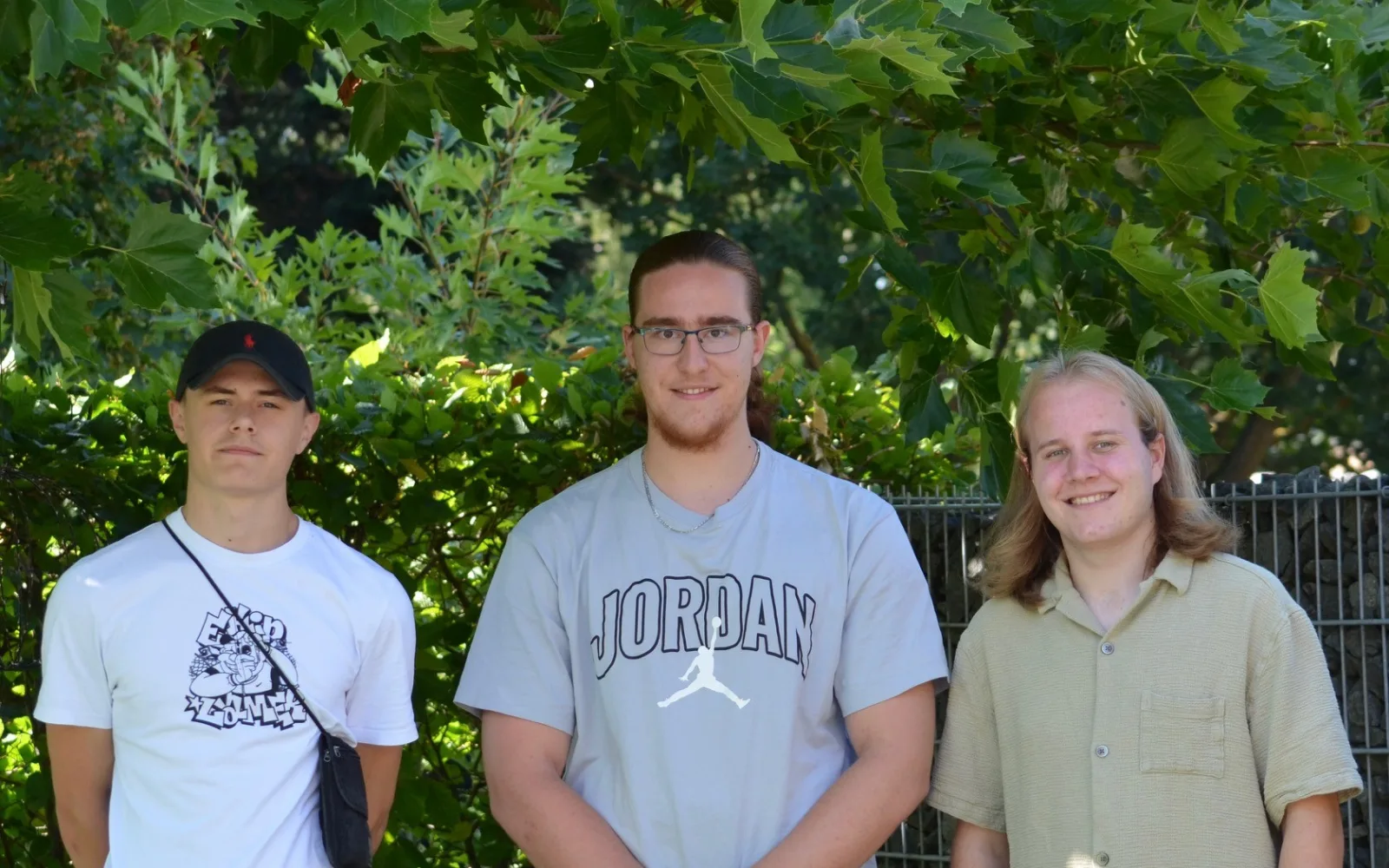 Drei junge Männer vor einer Hecke im Garten