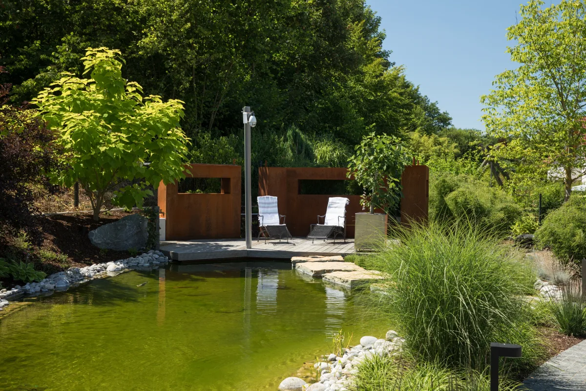 Blick über einen Schwimmteich auf eine Liegecke. 
