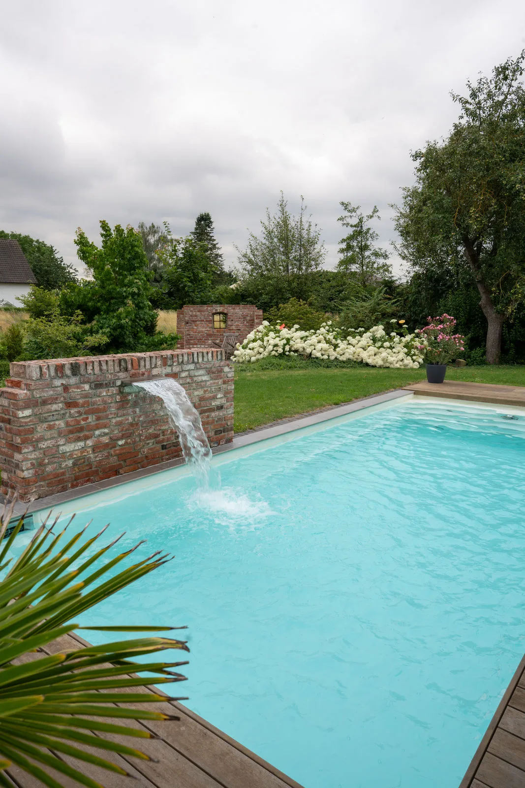 Draufsicht auf einen klassischen Chlorpool mit türkiesem Wasser und gemauertem Wasserfall.