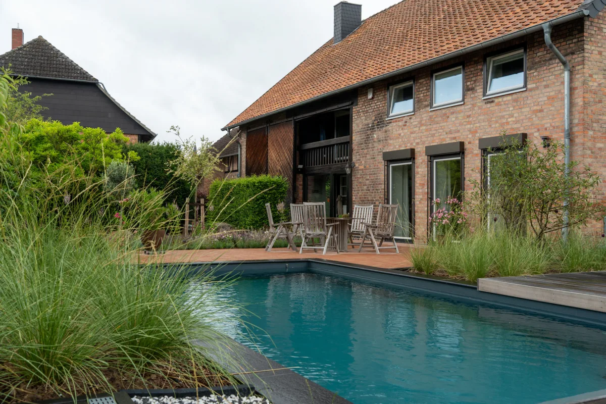 Blick über einen Naturpool auf Gartenanlage mit Einfamilienhaus im Hintergrund.