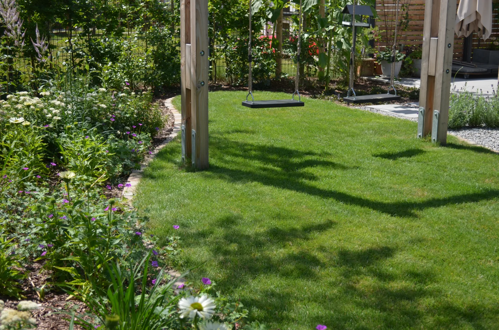 Blick in einen Garten mit Rasenfläche und einer Schaukel als Mittelpunkt.