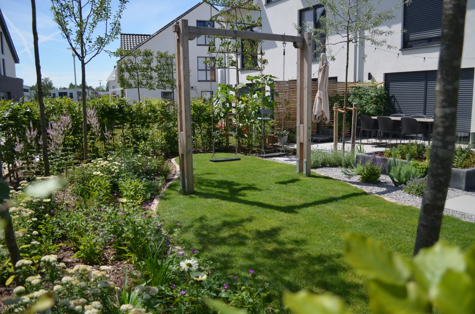 Garten mit Pflanzfläche, Rasen und Terasse.