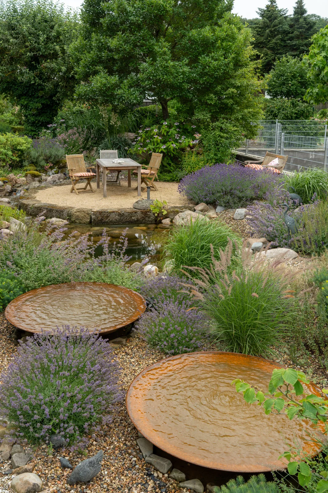 Komplettansicht des Gartens mit Wasserspielen, Gartenteich und Sitzinsel.